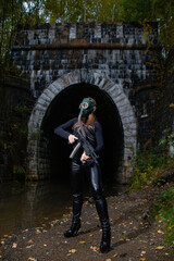 Fototapeta na wymiar a woman in a black suit and gas mask with a machine gun in her hands