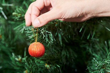 Hand of a young woman hanging a beautiful red and golden bauble