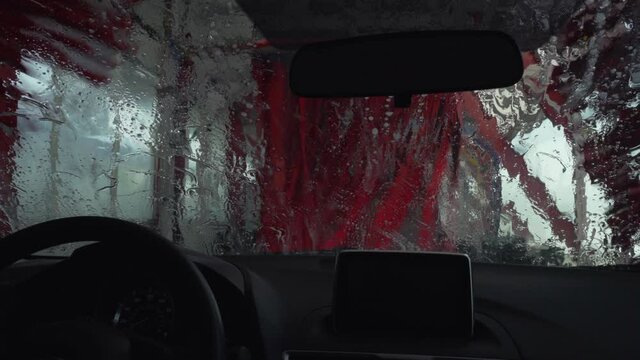 A car being cleaned by red wipers in a drive through car wash