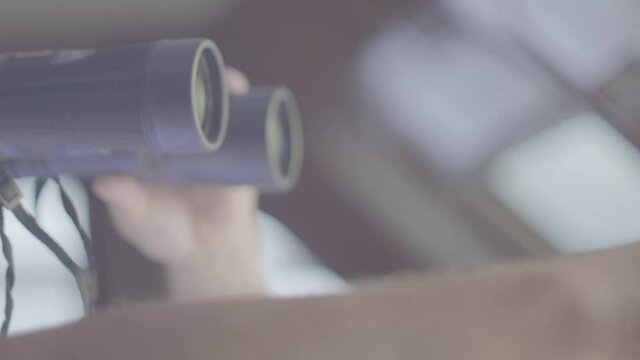 The hand of a man is pointing into some directions as he holds binoculars to see the horizon. The captain is holding binoculars.