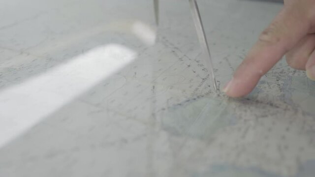 A captain is using a compass to calculate and measure the distance between two points on a map.