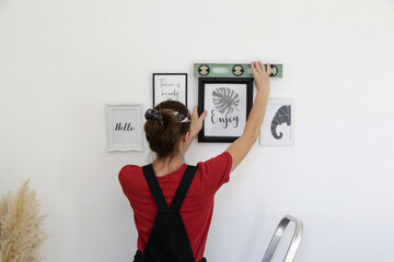 Woman arranging picture frames on wall in new house, diy home improvement concept