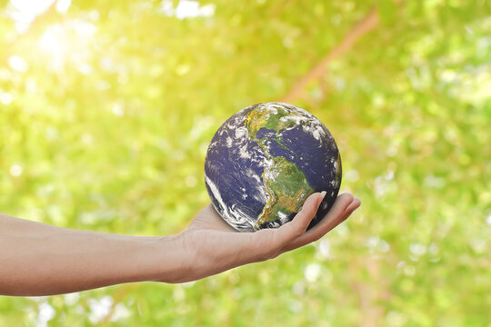Environment concept. Hand holding Earth against green spring background. Elements of this image furnished by NASA