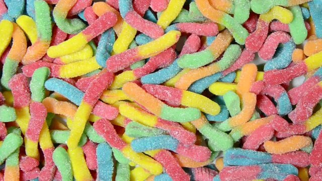 HD video zooming out from many colorful gummy worms coated in sugar, young caucasian female hand reaches in to remove a single gummy worm candy.
