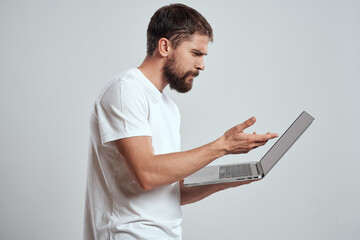 A man with a laptop in his hands on a light background in a white t-shirt emotions light background new technologies