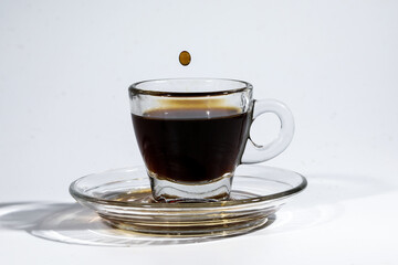 Coffee droplet on transparent glass espresso cup saucer full of liquid coffee on white background