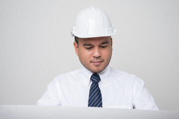 Young handsome asian civil engineer looking paperwork blueprint roll standing post in studio. Worker wearing hard hat on isolated white background..