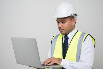 Asian civil engineer operate with laptop to control working in studio. Worker wearing hard hat using laptop computer standing on isolated white background.