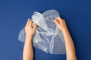 Hands popping a bubble wrap on classic blue background, antistress therapy concept, oddly...