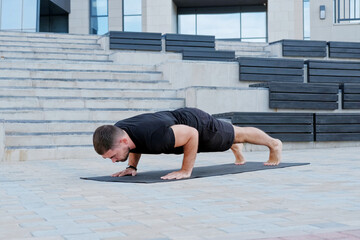 Fototapeta na wymiar Man athlete in black sportswear practices yoga exercises in plank position outdoors.