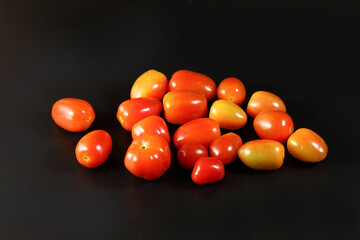 Fresh ripe small shiny red tomato on black background