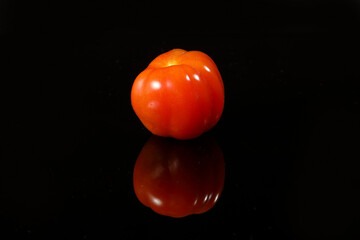 Fresh ripe small shiny red tomato on black background