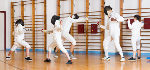 Adults and teens wearing fencing uniform practicing with a foil in a gym
