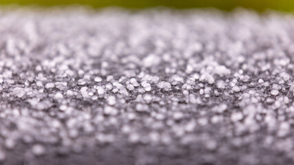 Up close view of a pieces of hail covering black metal surface