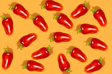 Vegetable pattern. Repetition of red peppers on an orange background. Top view of a whole red bell pepper. Horizontal. The concept of healthy food and vegetarianism.