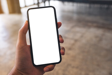 Mockup image of a man holding black mobile phone with blank white screen in cafe