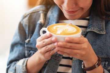 Closeup image of a beautiful young asian woman holding and drinking hot coffee in cafe