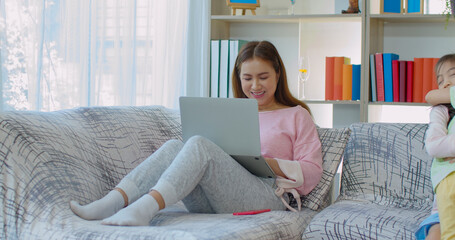 Young mother working on laptop with two daughter on sofa