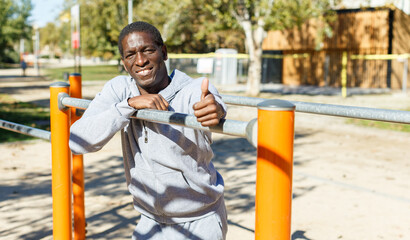 Athletic african american male performs warm-up exercises at chin-up bar in park