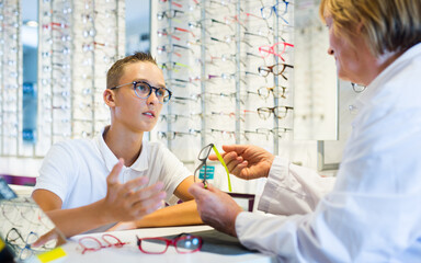 Fototapeta premium Female ophthalmologist and cheerful young boy choosing glasses in optics store