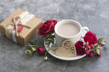 on a dark gray background: gift box, cup of coffee with milk, red rose and sprigs of eucalyptus wooden carved heart. Greeting Card for Mother's Day, Valentine's Day.