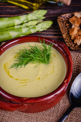 Fresh asparagus creamy soup and ingredients on a wooden table.