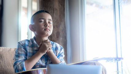 Cute boy praying to God in front computer laptop, Online church in home, Home church during...