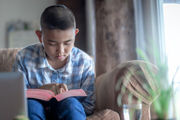 Young man sitting on sofa and raeding bible at home, Online church in home, Home church during quarantine coronavirus Covid-19, Religion concept.