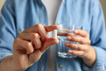 Woman hold glass of water and pill, close up