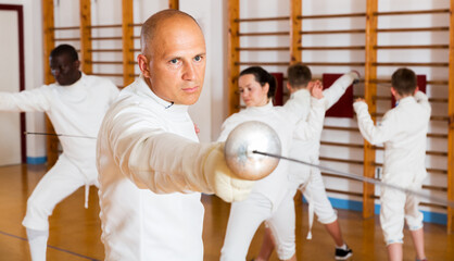 Man athlete training attack movements with rapier at fencing workout in gym