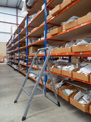Shelves in a warehouse full of material in small cardboard containers with a ladder to reach the material.
