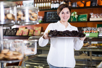 Young female seller offering tray of cakes with icing in confectionery