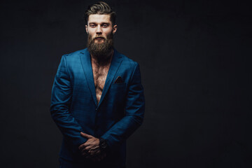 Bearded and mature businessman posing in blue suite with stylish haircut and serious face in dark background.