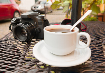 una taza de café como primer plano al exterior de una cafetería y una cámara en segundo plano....