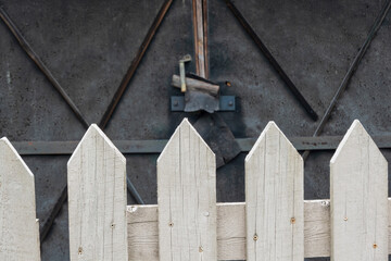 The top of the fence is in the foreground. There are pointed ends of white wooden planks. In the...