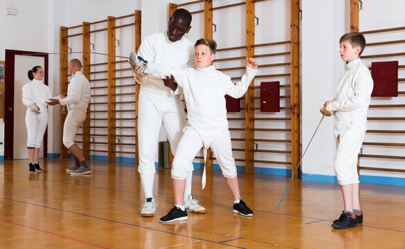 Trainer demonstrating to teenage athletes stances and movements with rapier during fencing workout