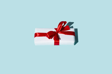 Christmas gift. Winter holidays surprise. Care package. Present wrapped in white box with red ribbon bow isolated on blue copy space background.