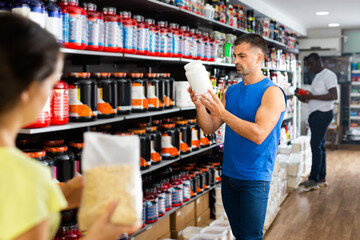 Portrait of positive athletic man choosing food supplements in large assortment of sport nutrition store