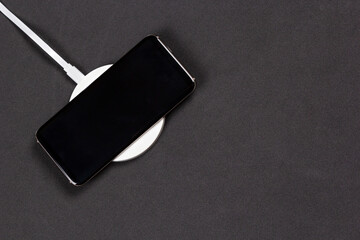 Wireless charging for phone on black background. Smartphone charges on fast induction charger.