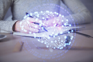 Double exposure of woman's writing hand on background with brain hud. Concept of learning.