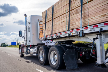 Classic big rig semi truck tractor transporting lumber on the flat bed semi trailer moving on the...