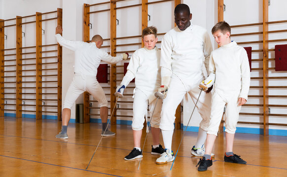 Coach demonstrating to teenage athletes stances and movements with rapier during fencing workout