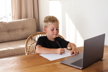 A blond boy draws from an online lesson. Distance learning. Copy space.