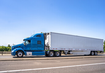 Side of blue big rig semi truck tractor transporting frozen cargo in refrigerator semi trailer...