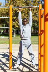 Fototapeta premium Athletic young male training different exercises at chin-up bar in park outdoor