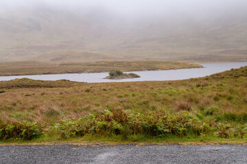 Small narrow asphalt road in Connemara and view on the mountains area and a lake. County Galway, Ireland, Low cloudy sky. Nobody