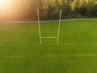 Fototapeta premium Aerial view on a green grass training pitch with tall goal posts at sunset, Field for popular Irish National sports: hurling, camogie, Gaelic football, rugby. Outdoors activity concept