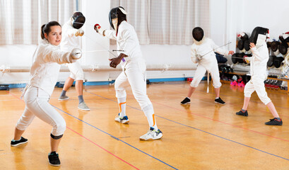 Fototapeta premium Young cheerful glad woman fencer practicing effective fencing techniques in training room