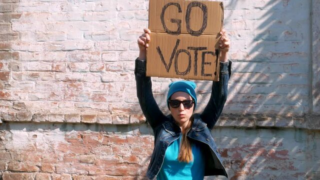 Woman shows cardboard with Go Vote sign on brick wall urban background. Honest voting concept. Make the political choice, use your voice. Youth voters invite to go to the presidential elections.