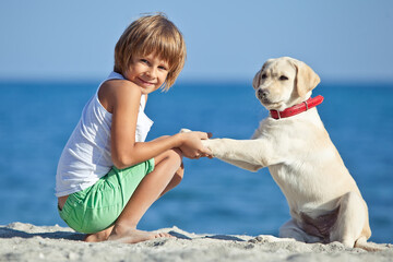 Happy boy playing with his dog on the seashore against the blue sky. Best friends have fun on vacation. High quality photo.